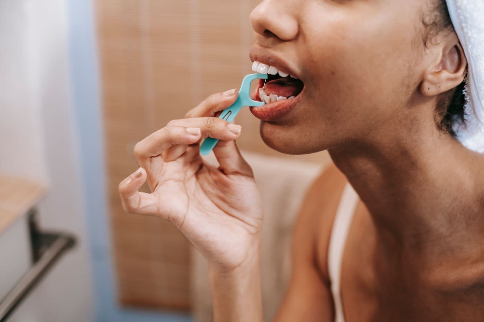 A woman using a floss pick to clean between her teeth in a bathroom