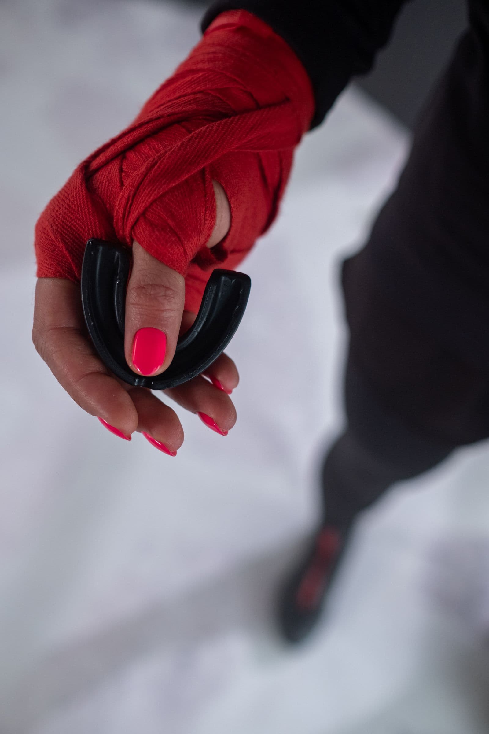 A hand wrapped in red boxing tape holding a black sports mouthguard