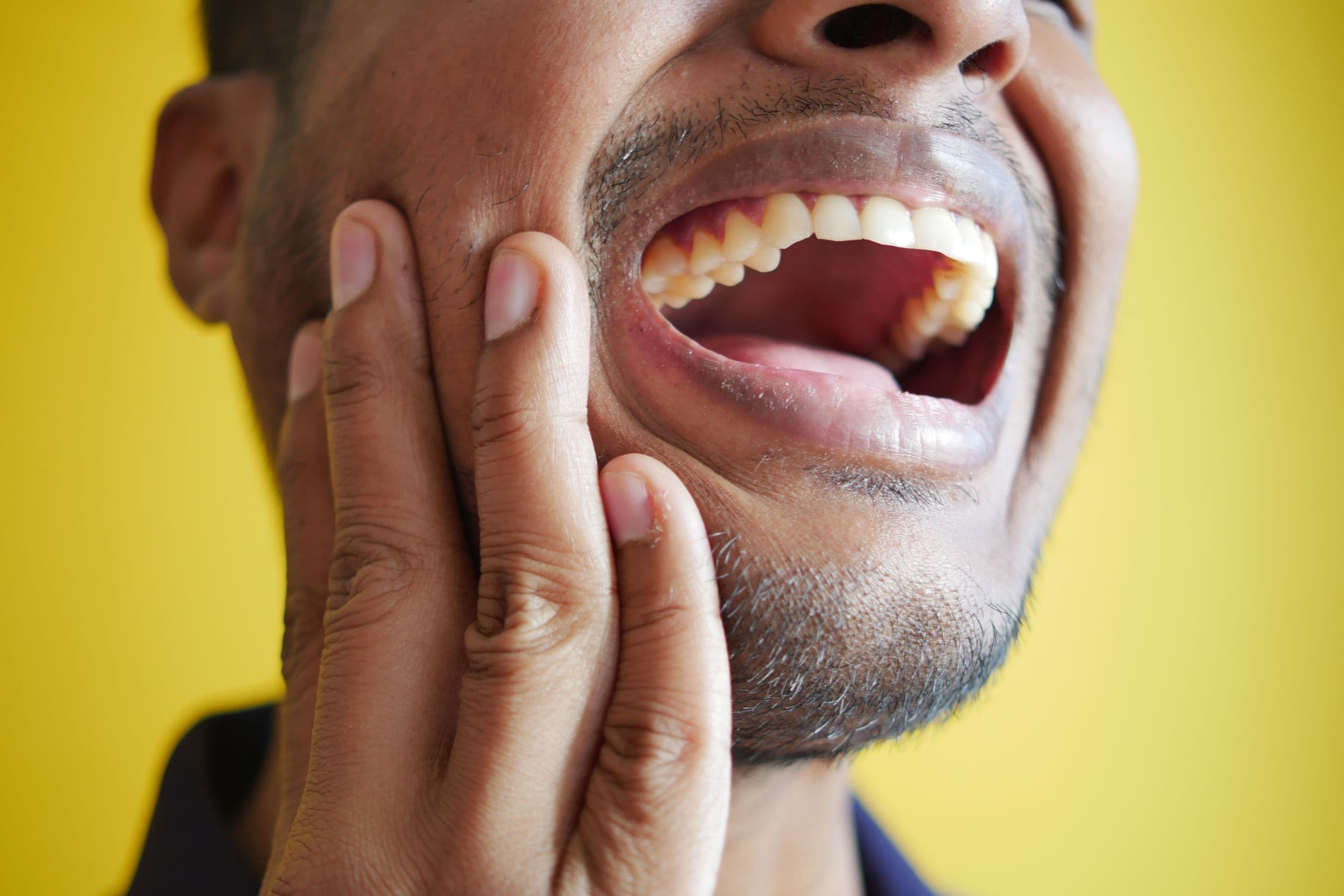 A person holding their jaw in discomfort, considering whether to seek urgent dental care