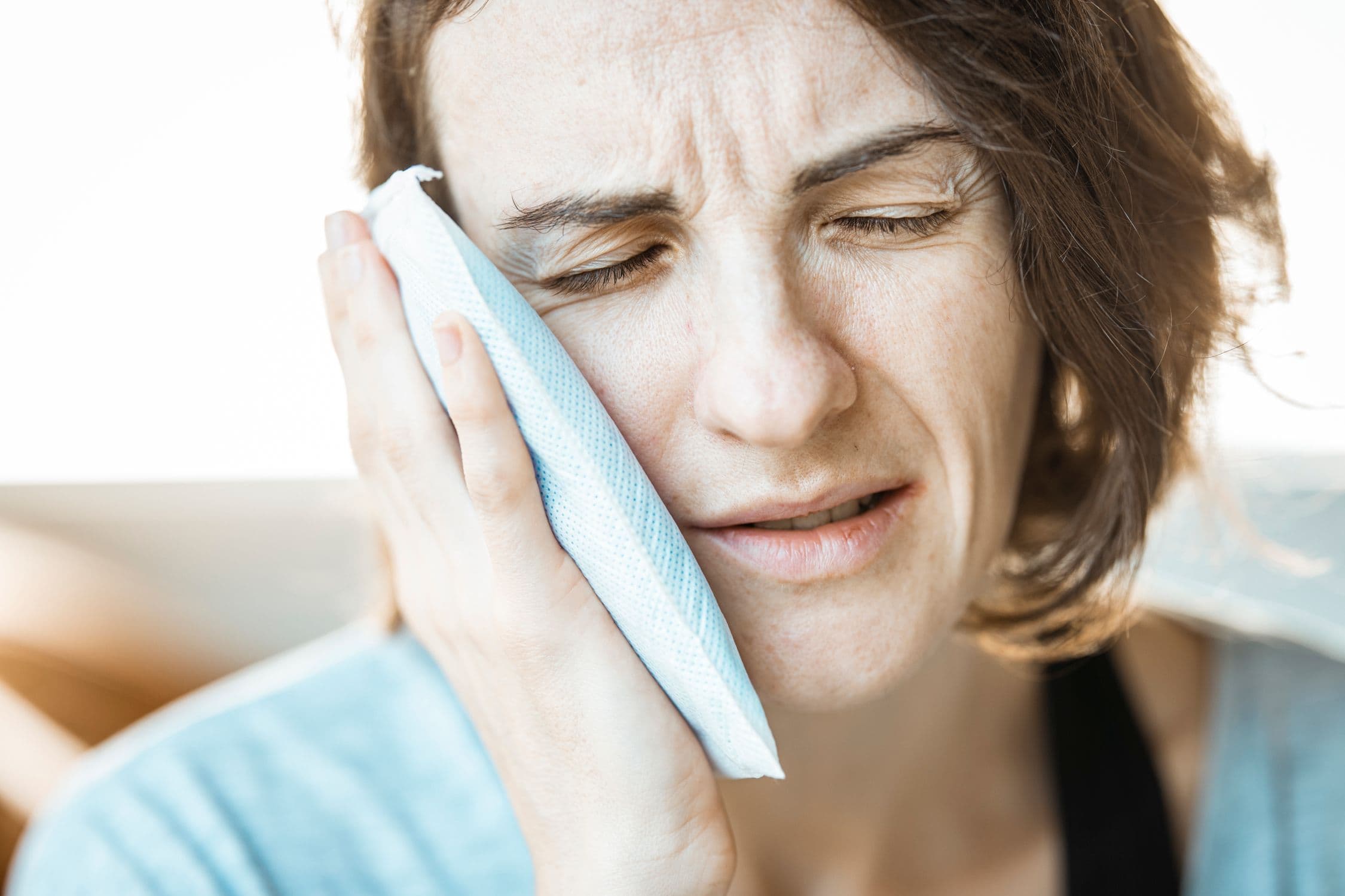 A person holding an ice pack against their cheek to manage dental swelling