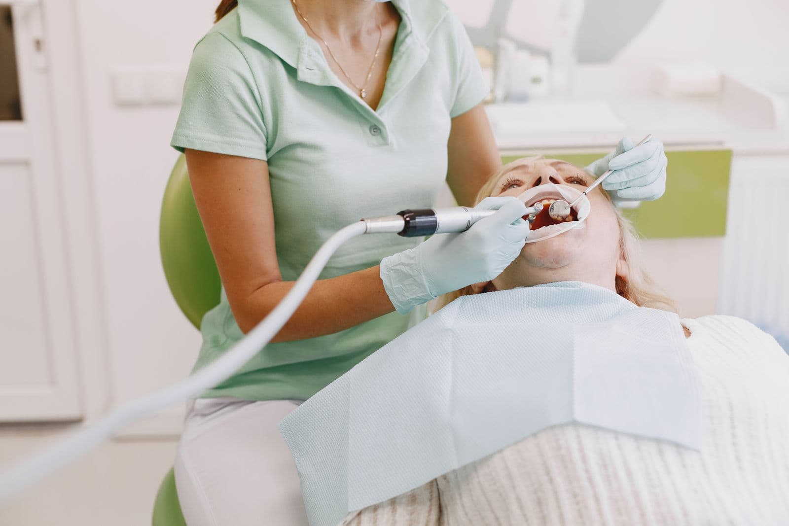 A dental professional in pale green scrubs treating a patient seated in a dental chair