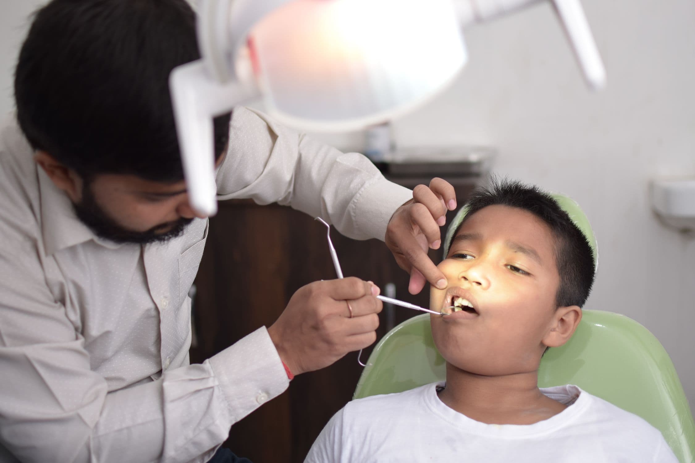 A dentist gently examining a young child's teeth while the child sits calmly in the chair